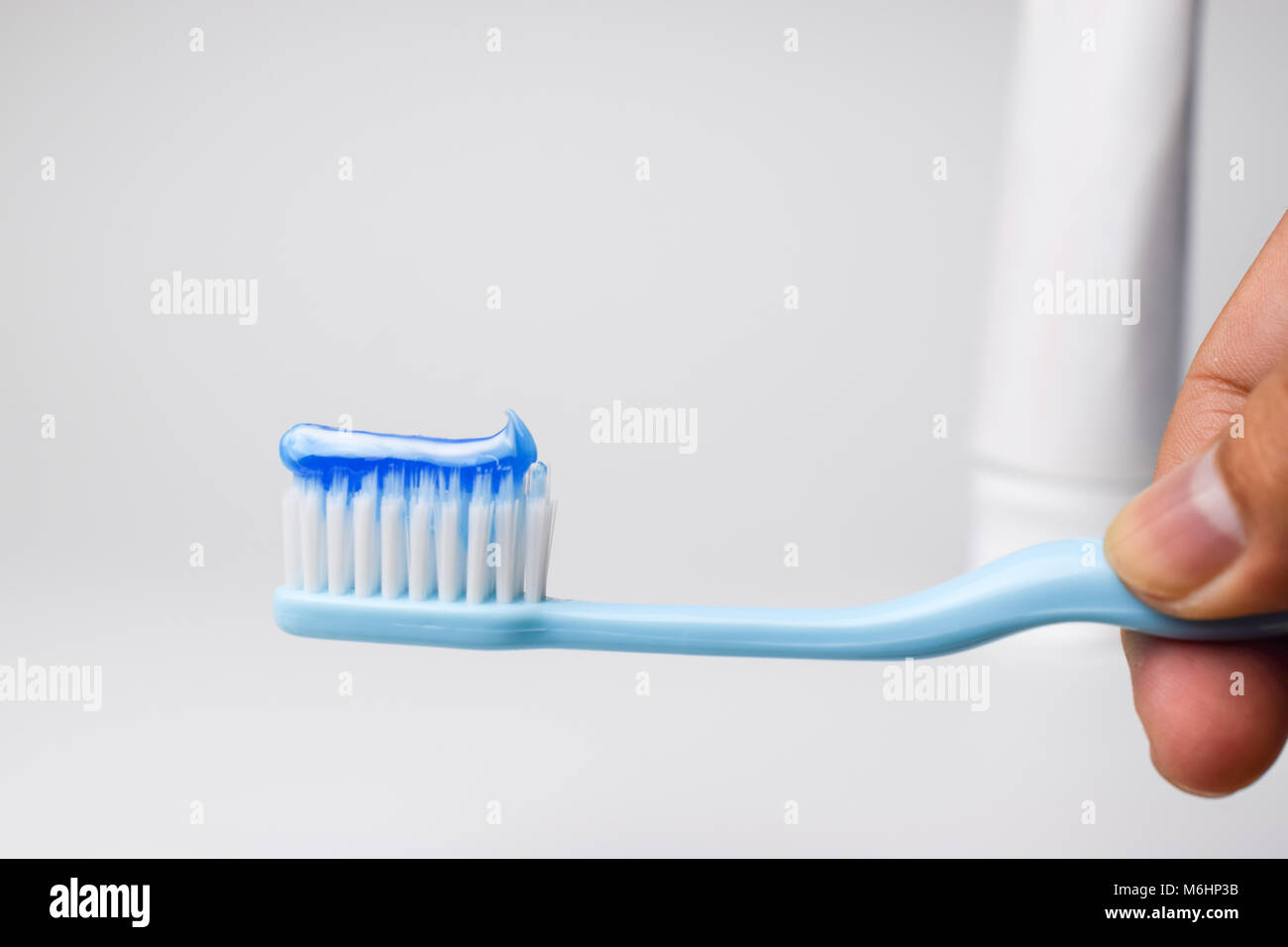 Hand holding a toothbrush with blue toothpaste on white background ...