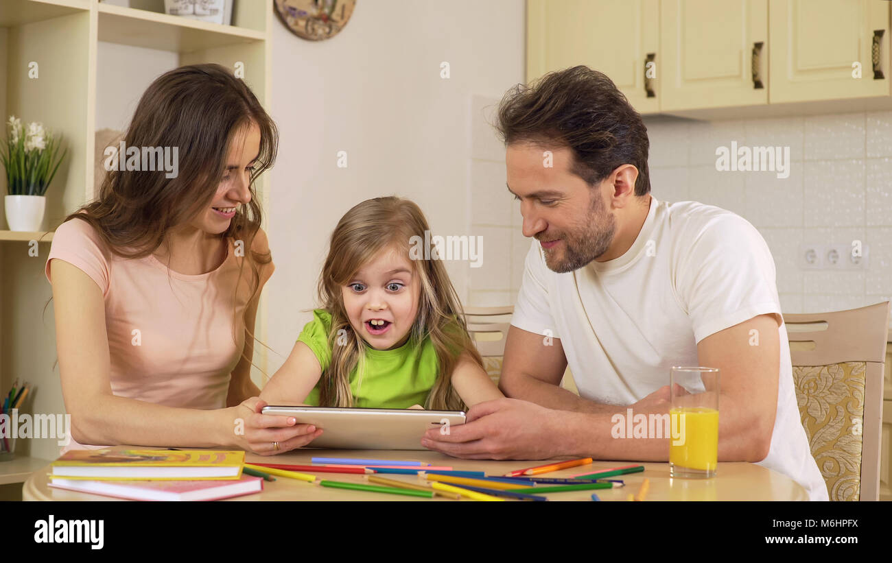 Parents showing daughter app on tablet, excited girl shocked and surprised Stock Photo