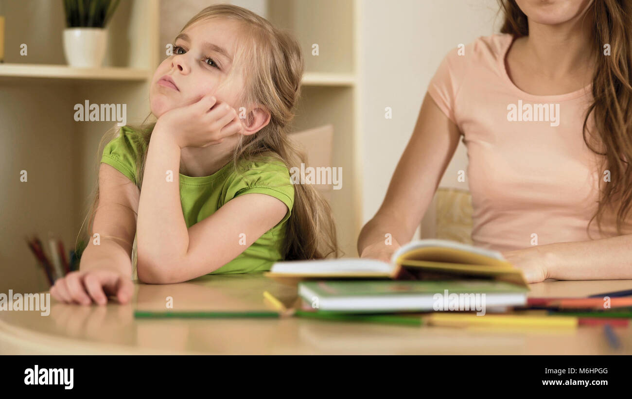 Sensitive mother hopelessly explaining homework to naughty daughter, disregard Stock Photo