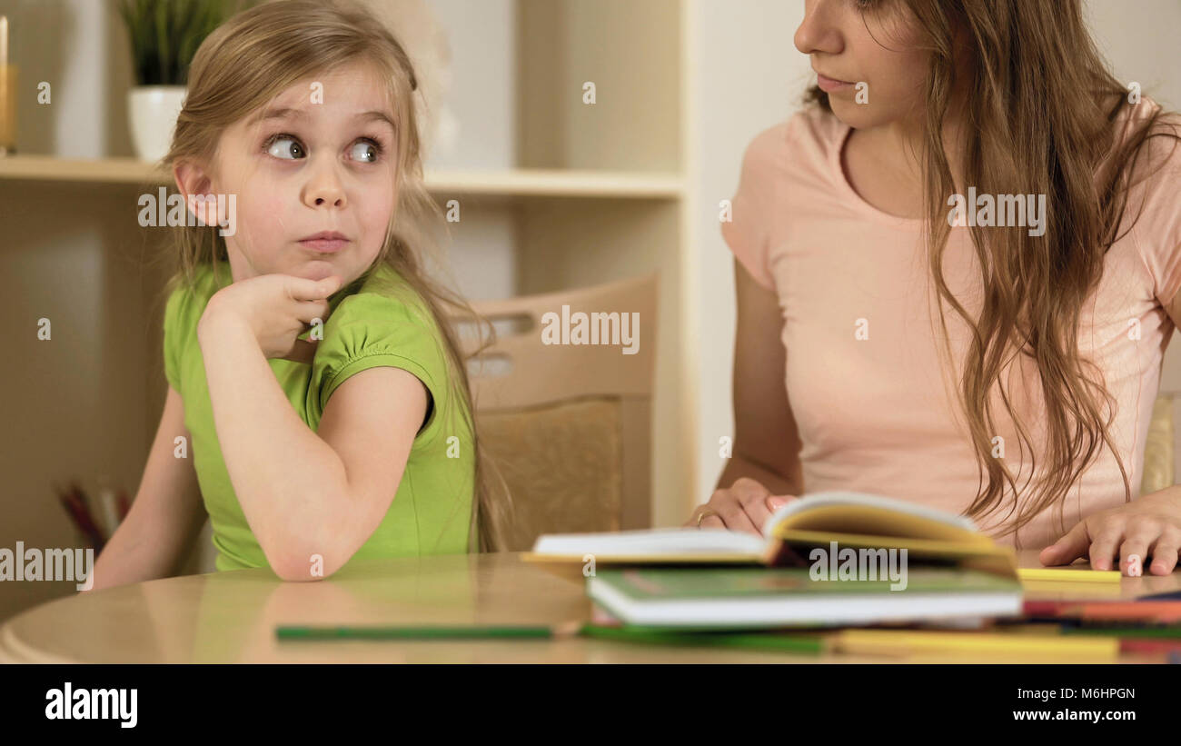 Bored daughter surprisedly looking to mother making her to do homework Stock Photo