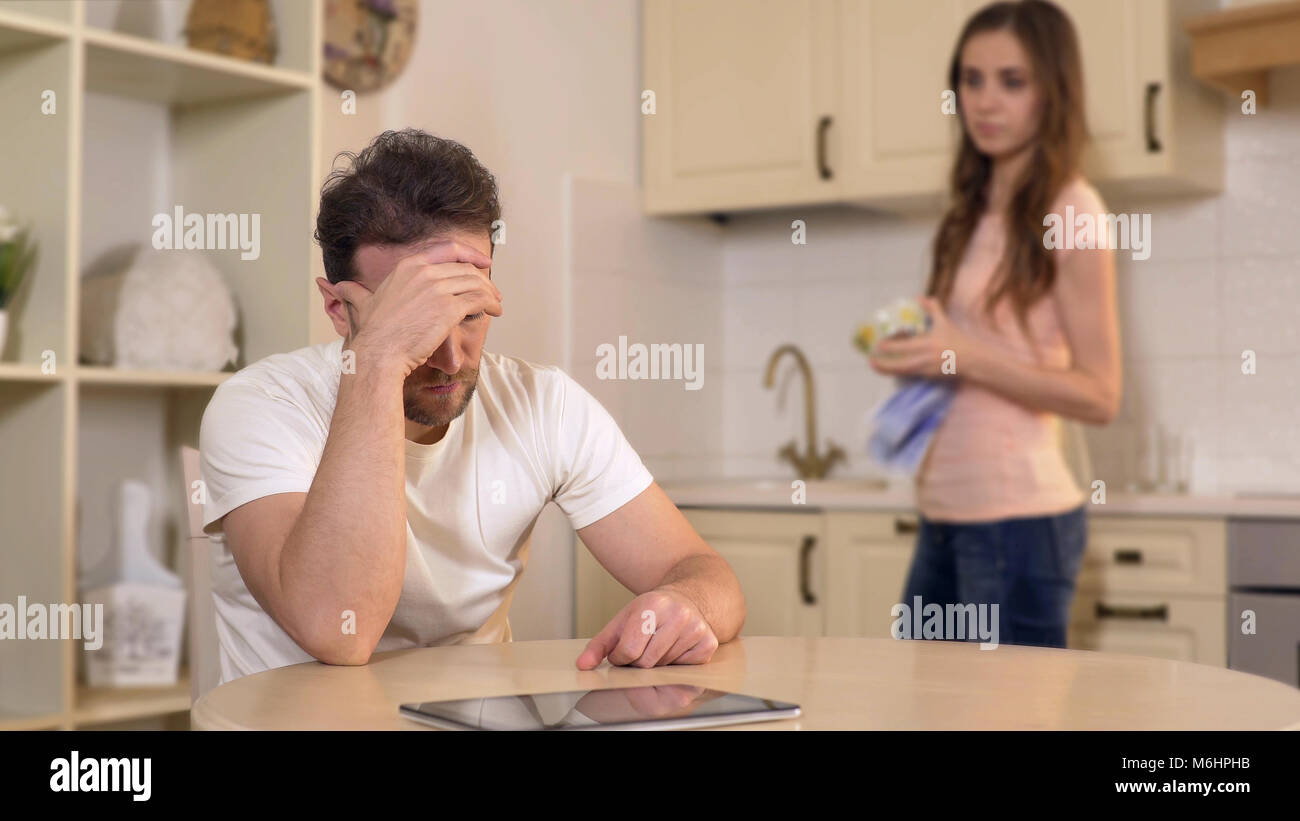 Wife scolding her unemployed husband at kitchen, chastising him for burning time Stock Photo