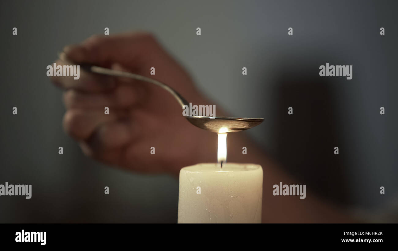 Hand of person heating chemical substance in spoon on candle light