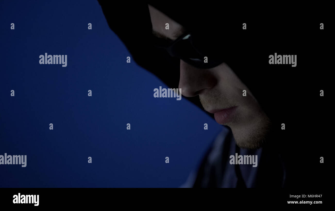 Male thief in hoodie and sunglasses, preparation before offense, face close up Stock Photo