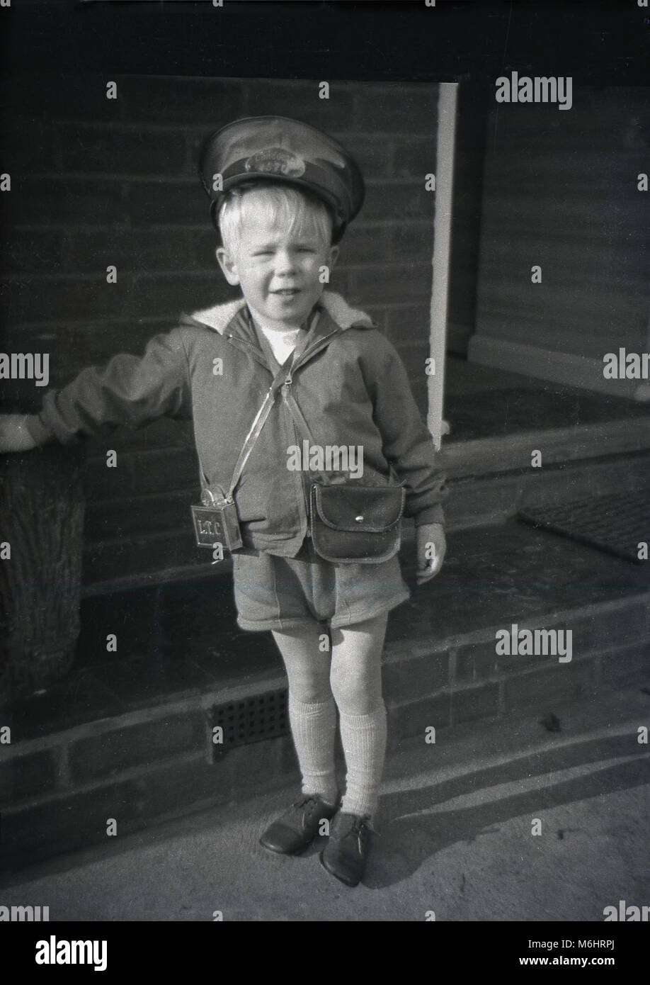 1960s, historical, young blond English boy standing outside wearing a bus conductor's set or outfit of cap, money bag and metal ticket punch, a popular child' dressing-up costume of this era. Stock Photo