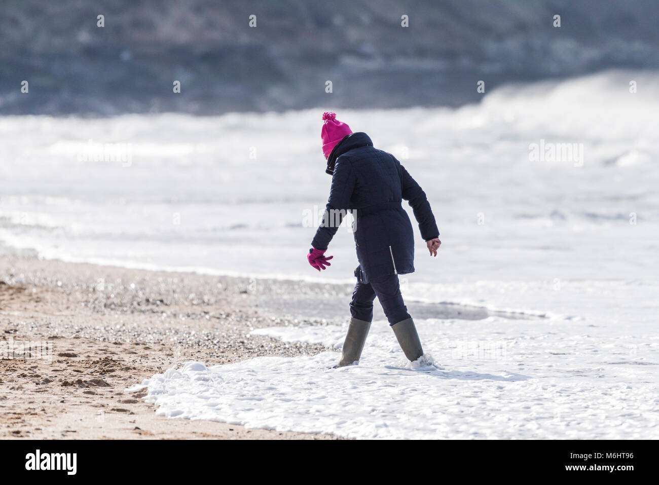 A woman wrapped up against the cold walking along the shoreline on Fistral beach in Cornwall. Stock Photo