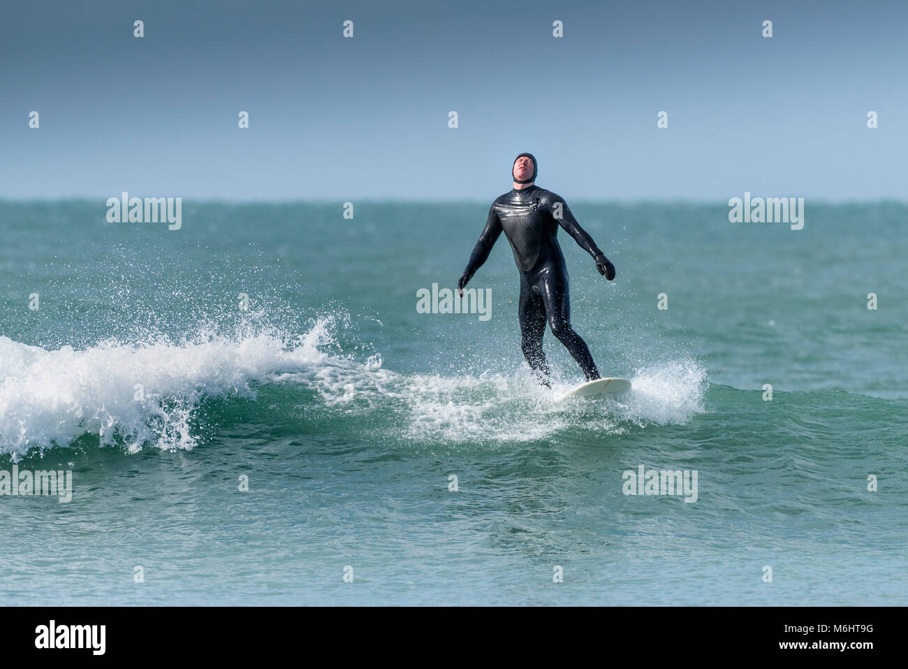 A surfer failing to ride a weak wave in cold wintry conditions at Fistral in Newquay Cornwall. Stock Photo