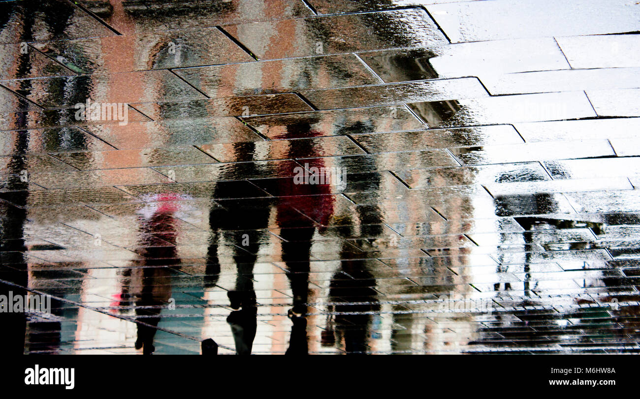 Blurry reflection shadow of people walking the city street patterned sidewalk on a rainy day Stock Photo