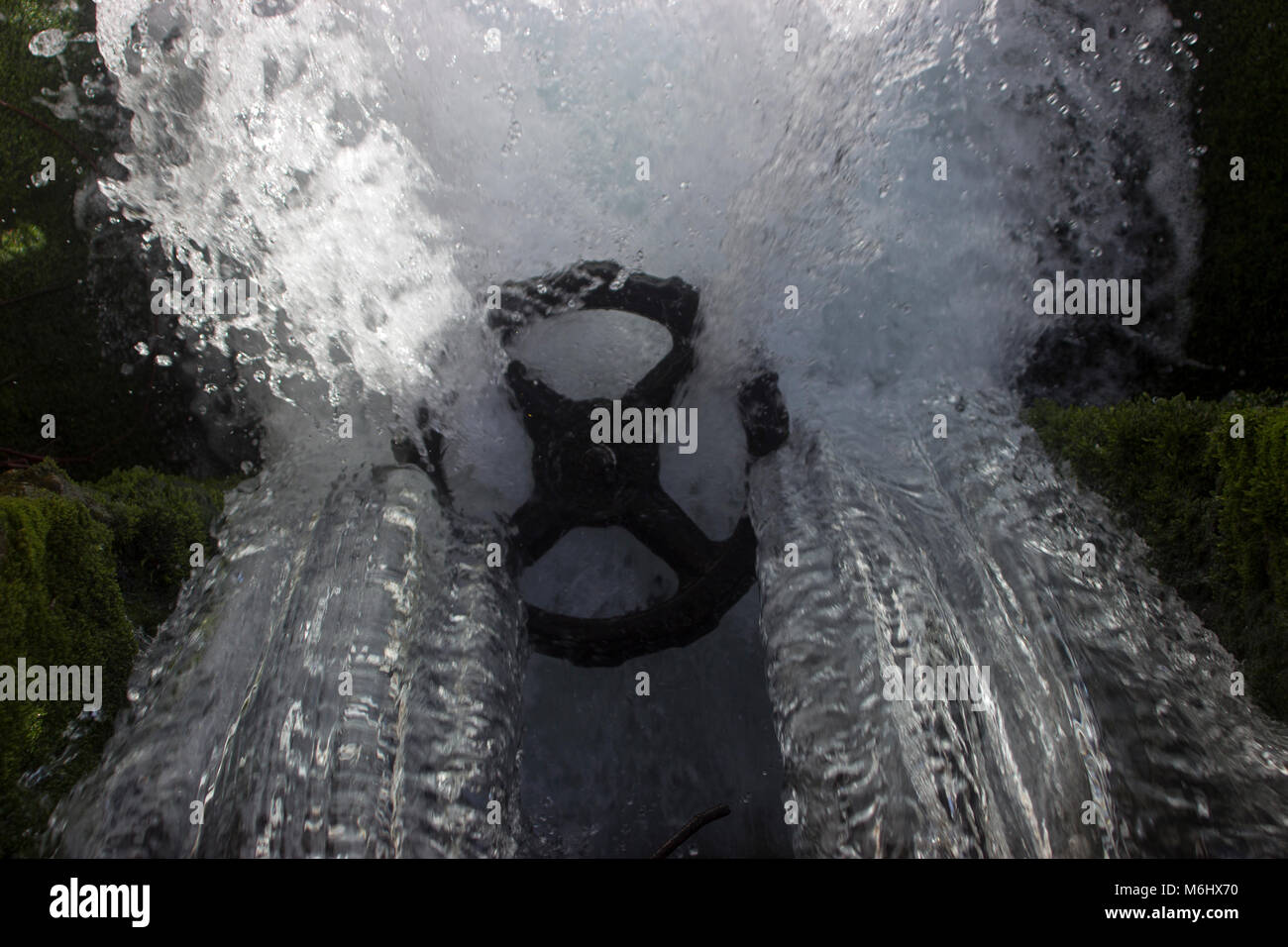Power of water. Water from a small waterfall flows trough a big iron wheel which is for regulating the stream Stock Photo