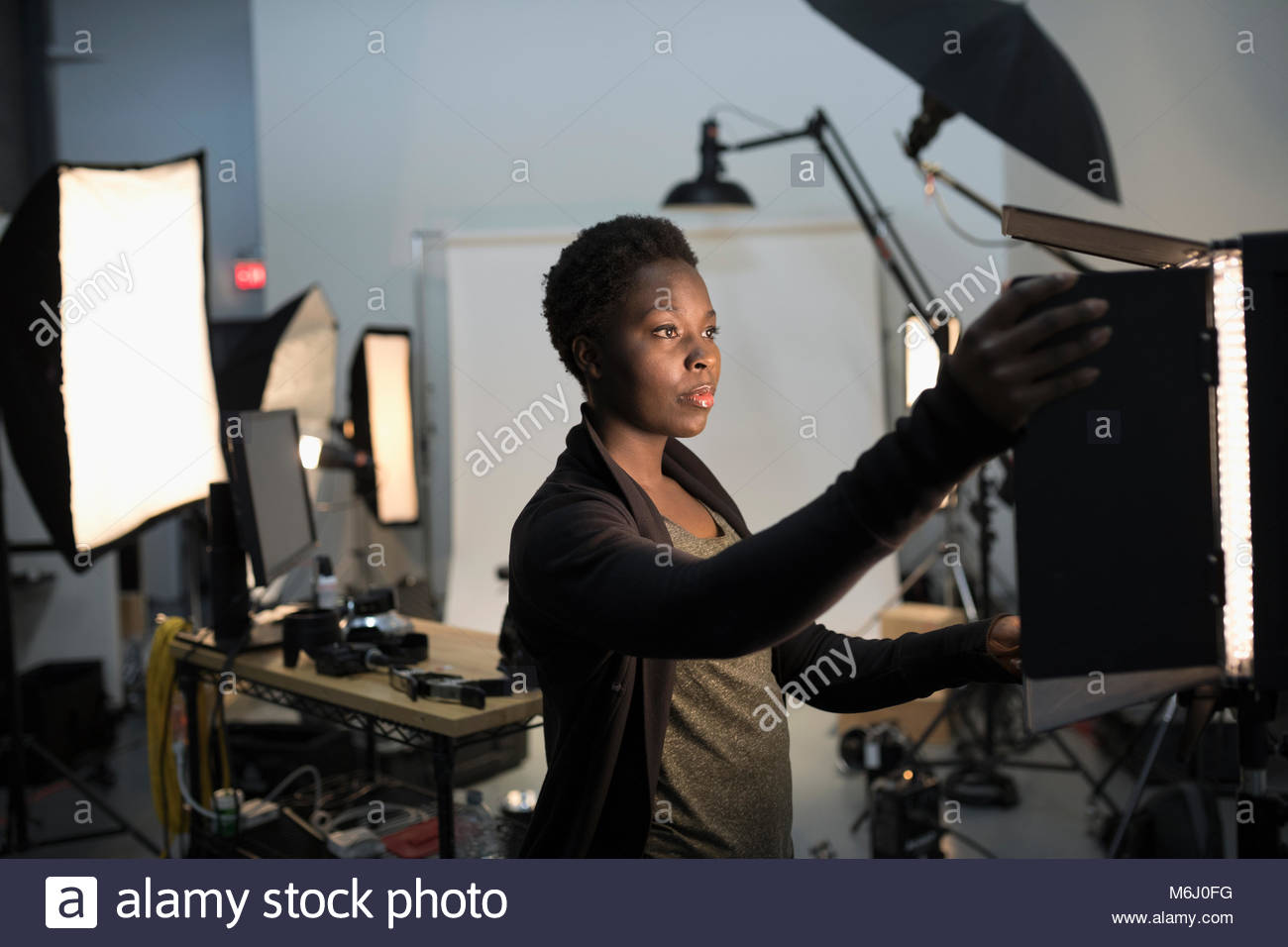 Focused female photographer adjusting lighting equipment for photo shoot in studio Stock Photo
