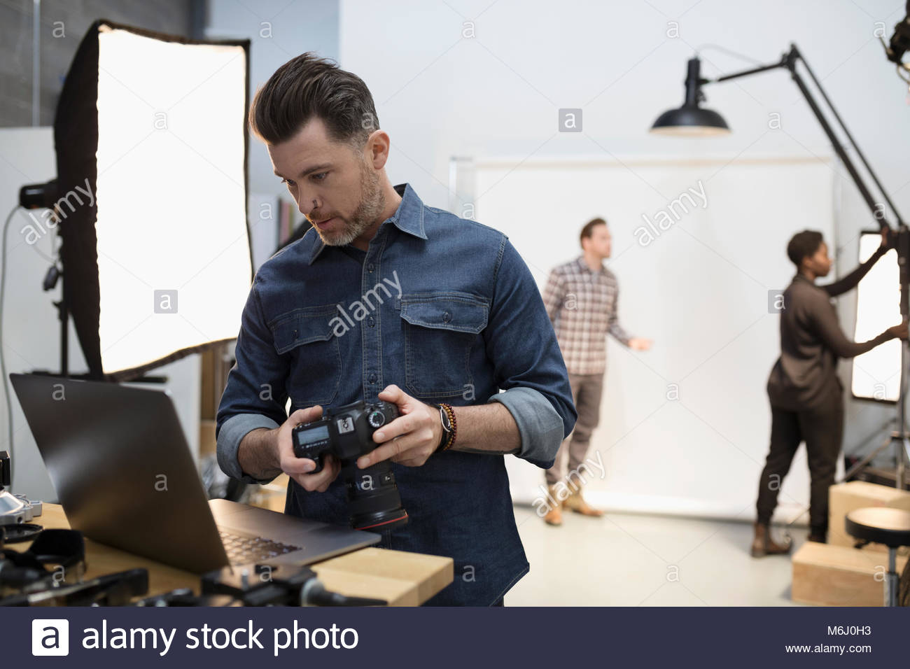Male photographer with digital camera using laptop at photo shoot in