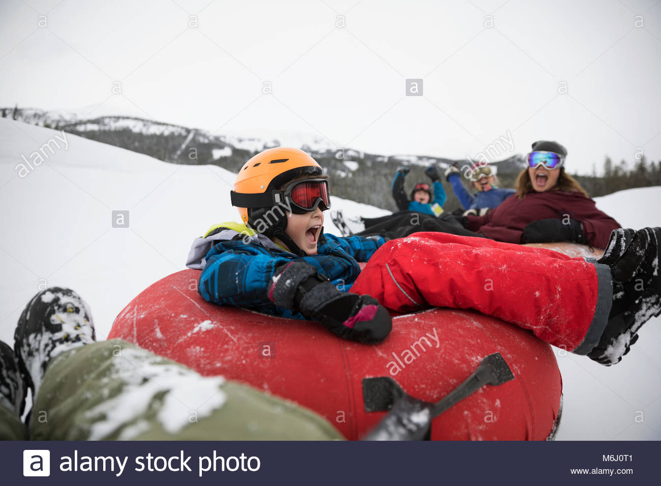 Playful boy inner tubing with family in snow at tube park Stock Photo