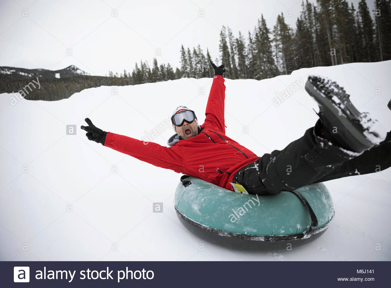 Portrait playful, exuberant man inner tubing in snow at tube park Stock