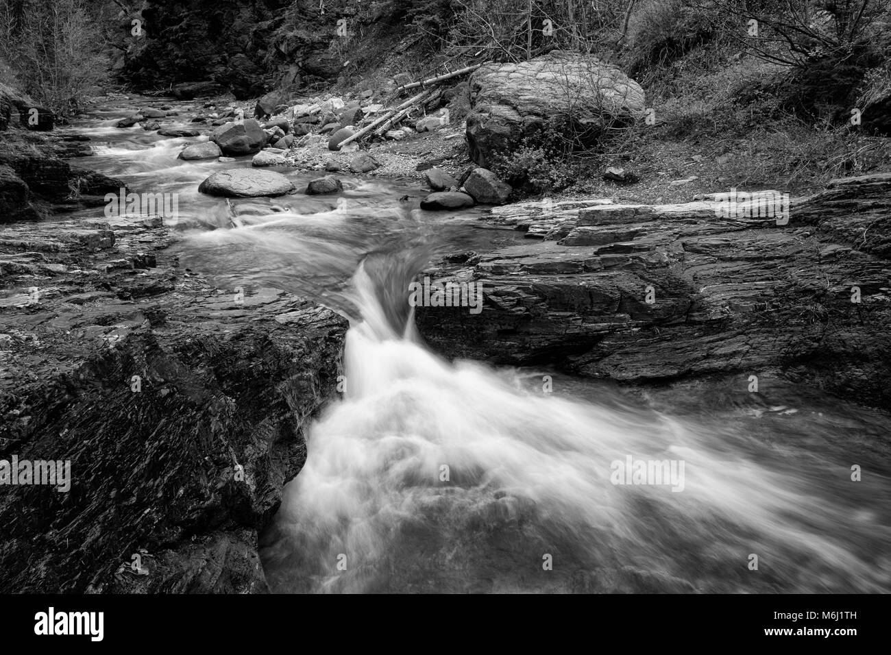 Beautiful soft time lapse grayscale water flowing over layered rock ledge  & boulders in Red Rock Canyon Waterton Lakes National Park Alberta Canada Stock Photo