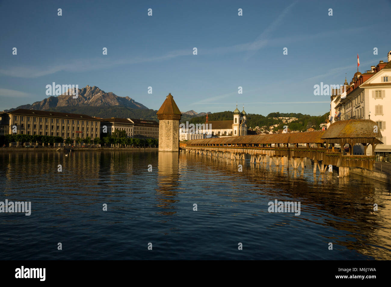 Beautiful light on ancient wood covered bridge reflected in lake  Lucerne Switzerland, tourist area Gutsch hotel, clock tower, masque, shops, blue sky Stock Photo