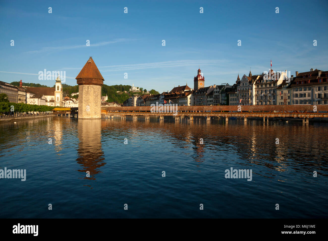 Beautiful light on medieval wood covered bridge reflected in lake,  downtown Lucerne Switzerland Gutsch hotel, clock tower, masque, shops, blue sky Stock Photo
