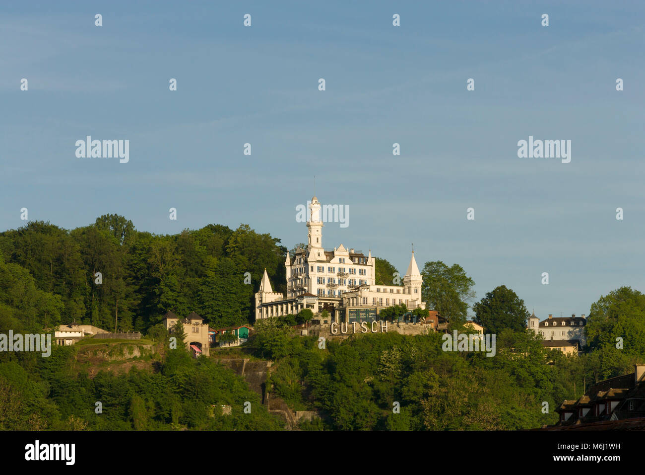 Famous 5 star luxury castle Hotel Gutsch sits high on hill above Lucerne Switzerland surrounded by green forest blue sky background Pan negative space Stock Photo