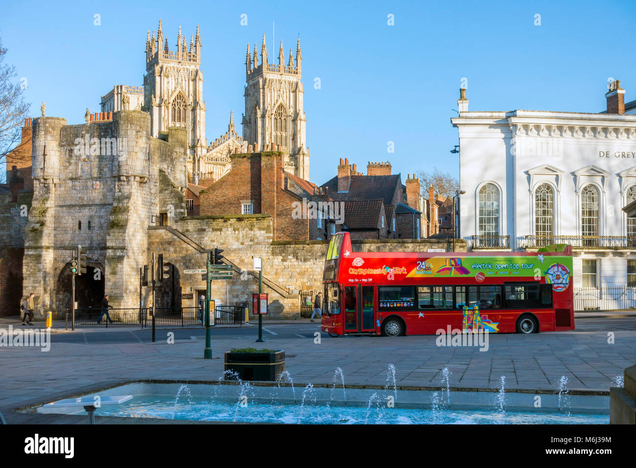 A bright red open topped double decker bus which takes tourists on a tour around York in Exhibition Square in front of Bootham Bar and the Minster Stock Photo