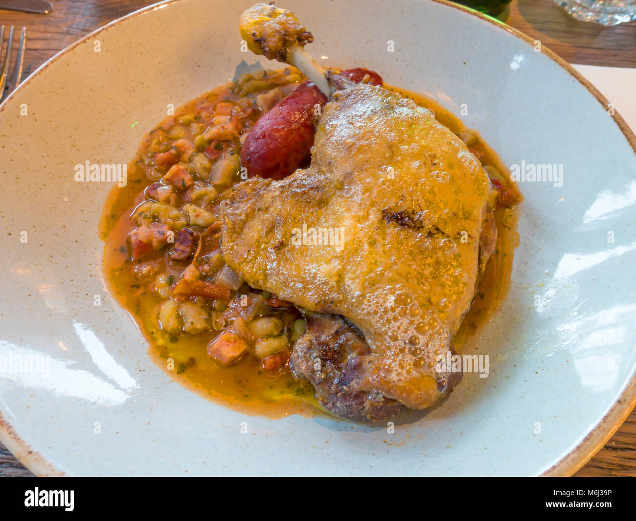 Lunch of duck leg confit with a cassoulet of Toulouse sausage, smoked bacon, flageolet beans and plum tomatoes Stock Photo