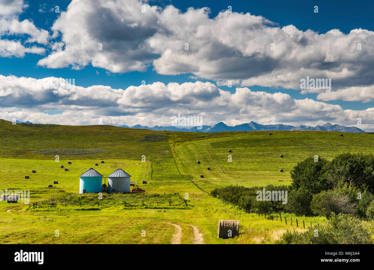 Small silos, bales of hay at ranch in rolling foothills of the Rocky Mountains, visible in far distance, near Longview, Alberta, Canada Stock Photo
