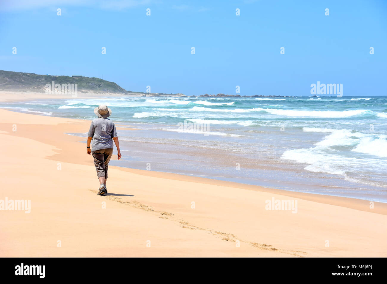 A female on a clean beach at Goukamma near Knysna on the garden route in South Africa walking determined and with energy with foot steps in the sand,  Stock Photo