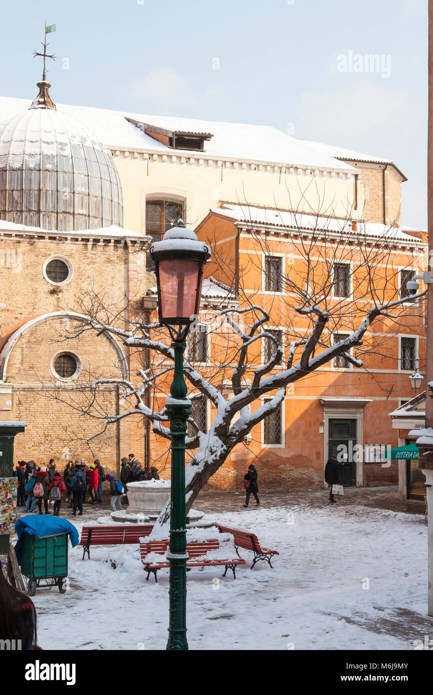 Winter snow in Campo dei Santi Apostoli, Cannaregio, Venice, Veneto, Italy covering the Santa Apostoli church, benches and tree with a tour group out  Stock Photo