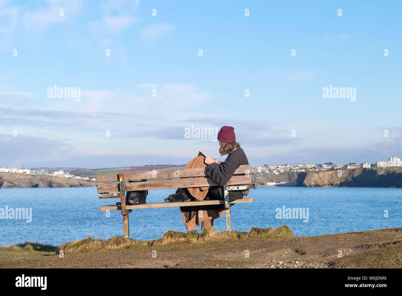 A woman sitting alone on a bench reading a book at Little Fistral in Newquay Cornwall. Stock Photo