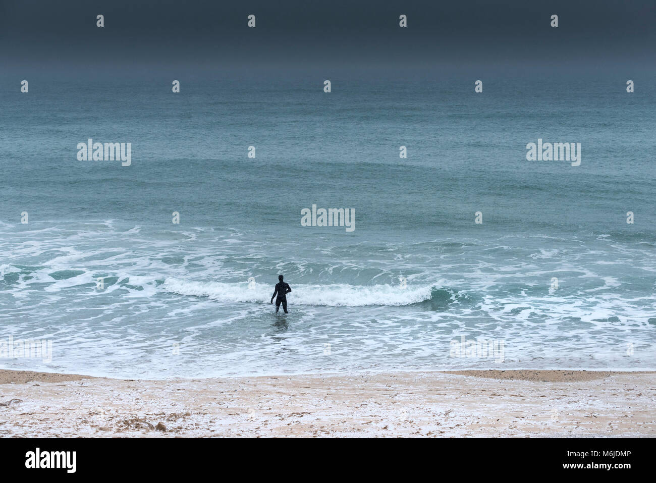 A figure in a wetsuit walking into the sea during freezing cold weather conditions. Stock Photo