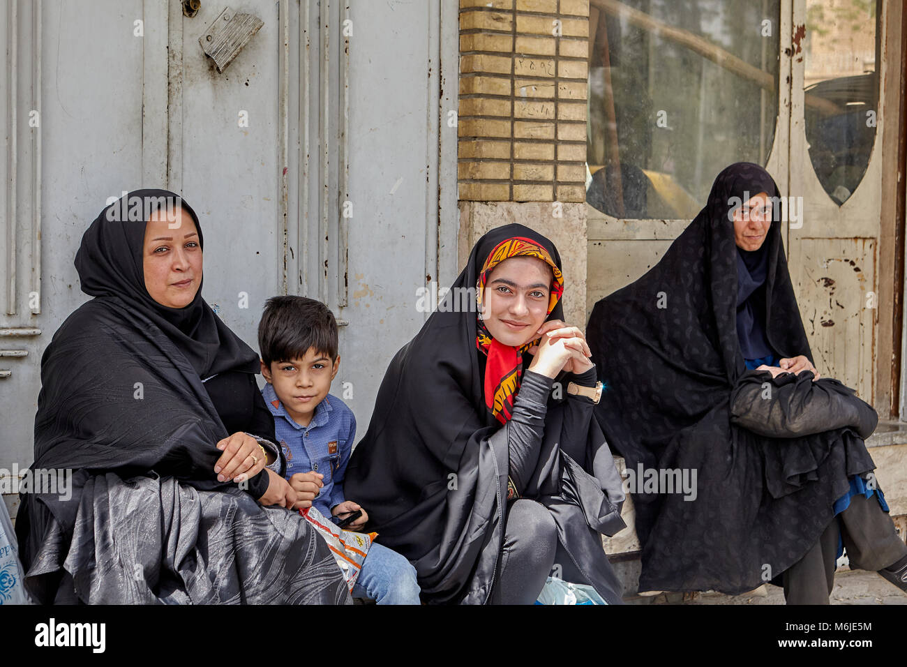 Kashan, Iran - April 27, 2017: Three women dressed in black Islamic clothes, and one little boy waiting for the municipal bus at a public transport st Stock Photo