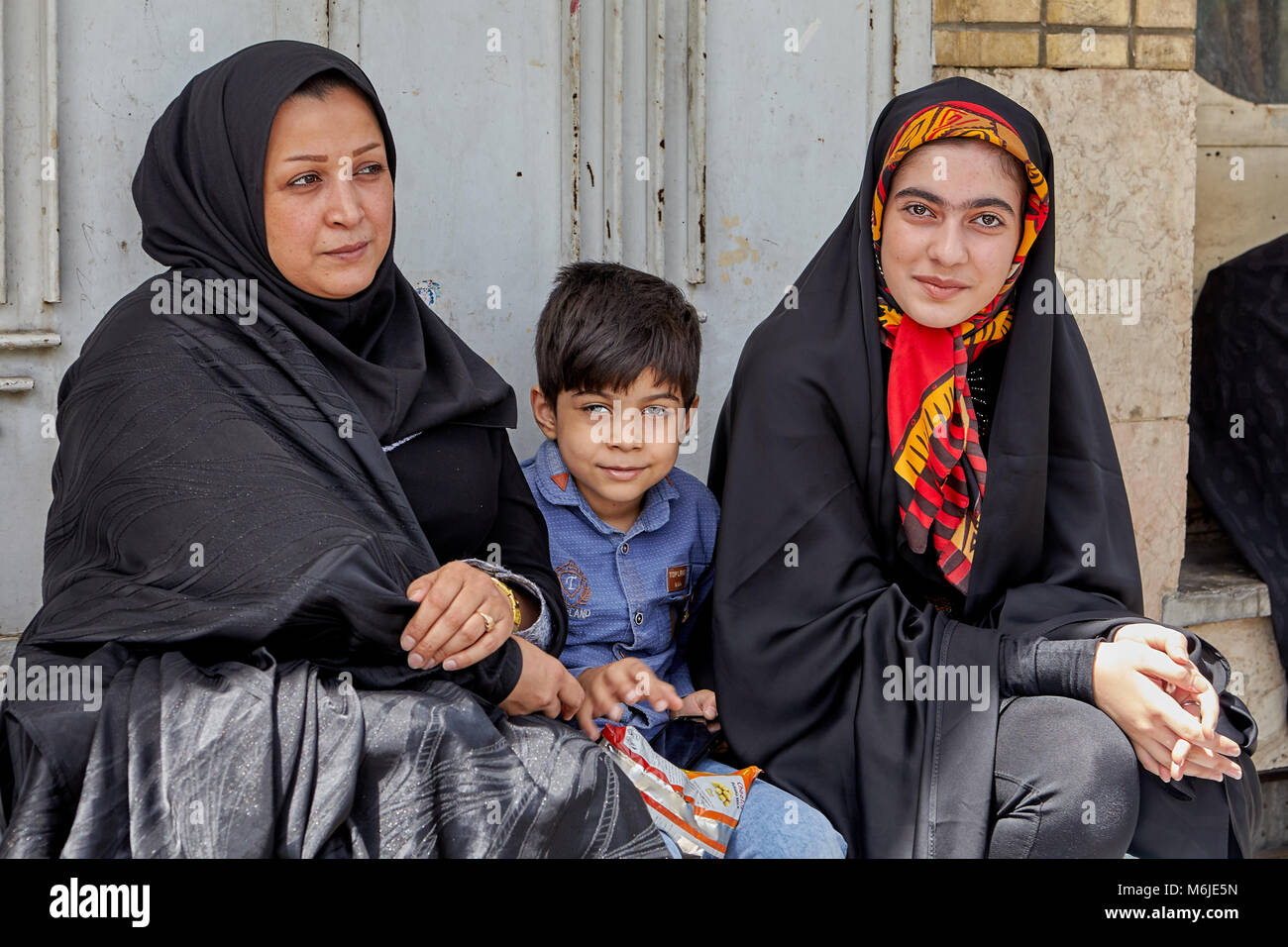 Kashan, Iran - April 27, 2017: A Muslim family, two women and one young boy, are waiting for the municipal bus at a public transport stop. Stock Photo