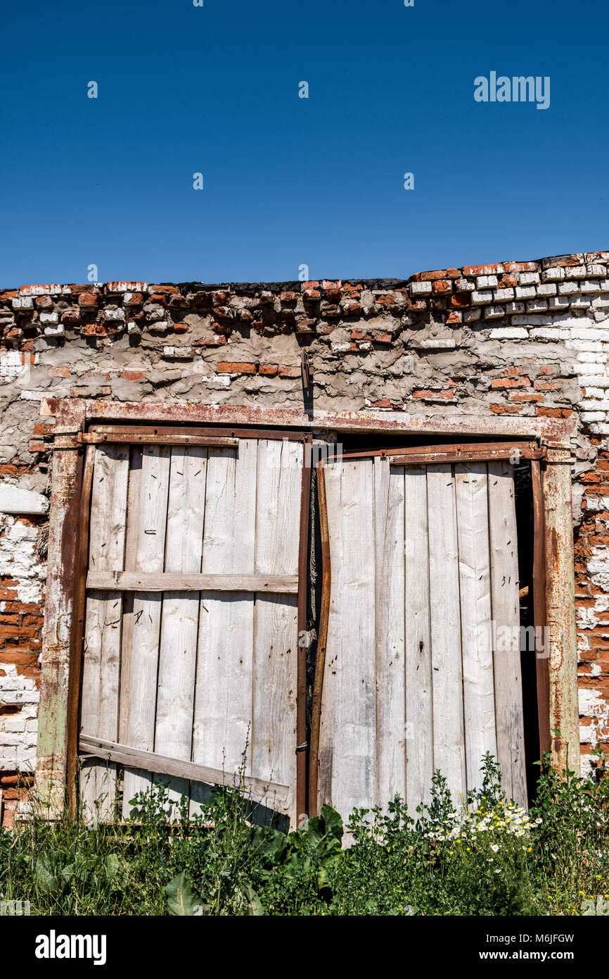 Abandoned old cowshed of weathered brick wall and with dilapidated wooden gate on sunny day in the countryside Stock Photo