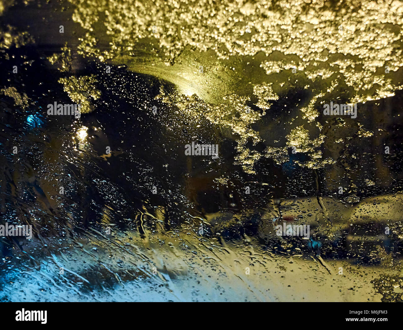 Raindrops and melting snow on the car window at night illuminated by