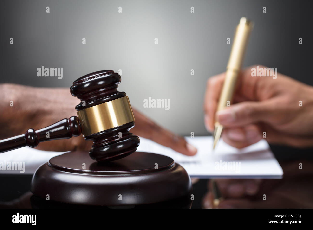 Close-up Of A Gavel With Person's Hand Signing Legal Document On Wooden Desk Stock Photo
