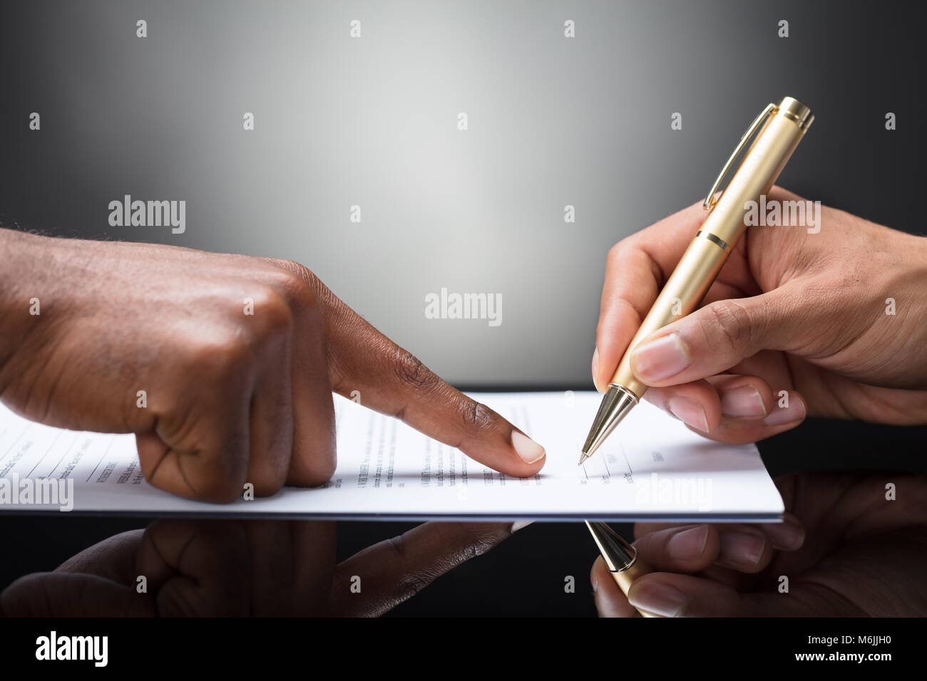Pointing The Finger In Front Of A Person Signing With Golden Pen On The Document Stock Photo