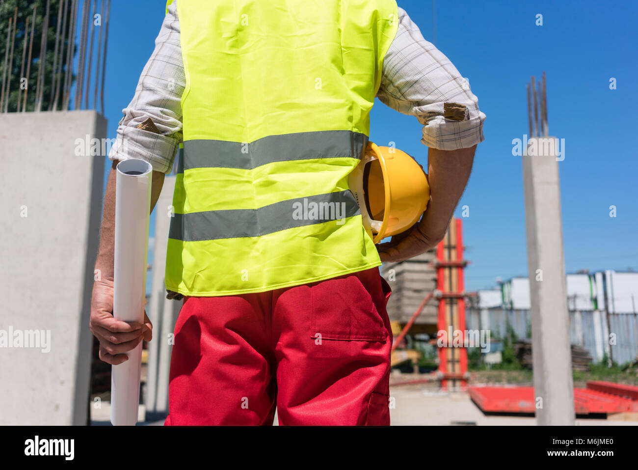 Midsection rear view of a worker holding a blueprint and a yellow hard hat Stock Photo