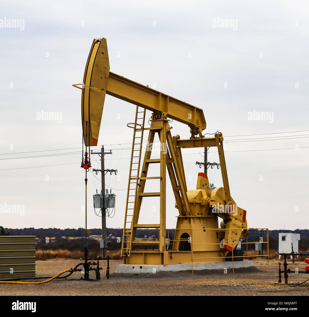 Large Yellow 912 Pump Jack on oil or gas well with surrounding equipment against an overcast sky Stock Photo