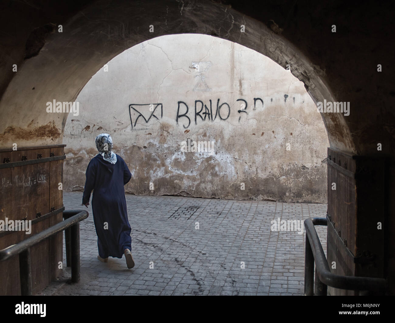 A woman, wearing traditional dress and a headscarf walks through an archway in the medina of Marrakech, Morocco. Stock Photo