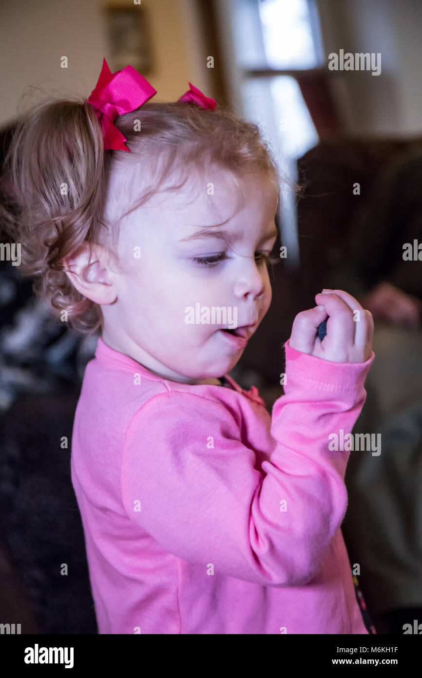 1 year old girl eating blueberries, one of her favorite foods, staring