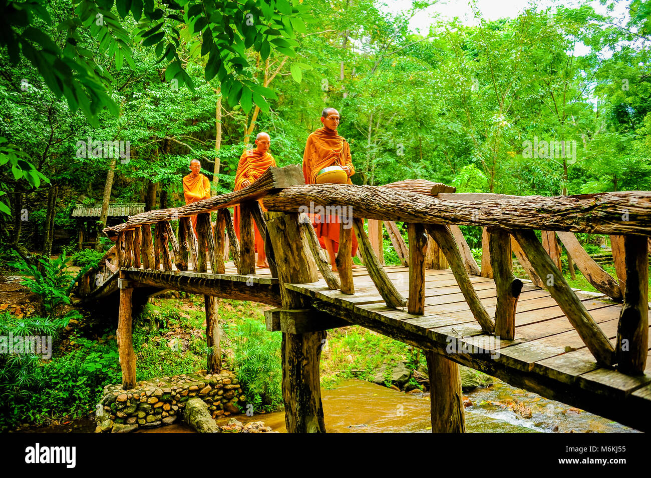 Kanchanaburi, Thailand - July 14, 2012: Buddhist monks marching on wooden bridge to seek alms in morning. This is usual every day duty of Buddhist mon Stock Photo