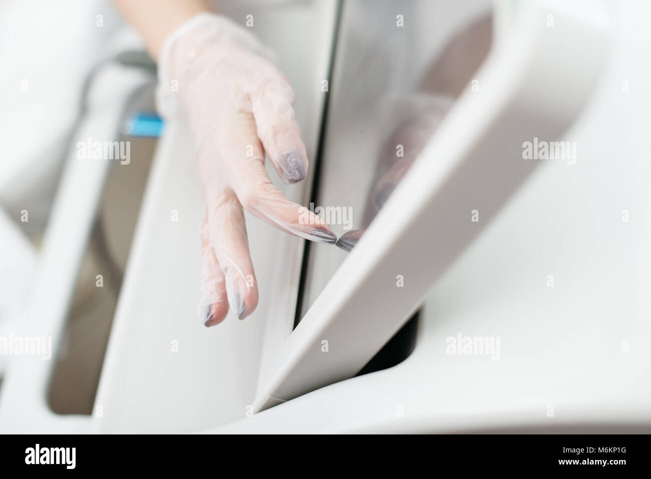 Female hands in polyethylene gloves touching the screen of laser apparatus to turn it on. No face. Close-up. Stock Photo