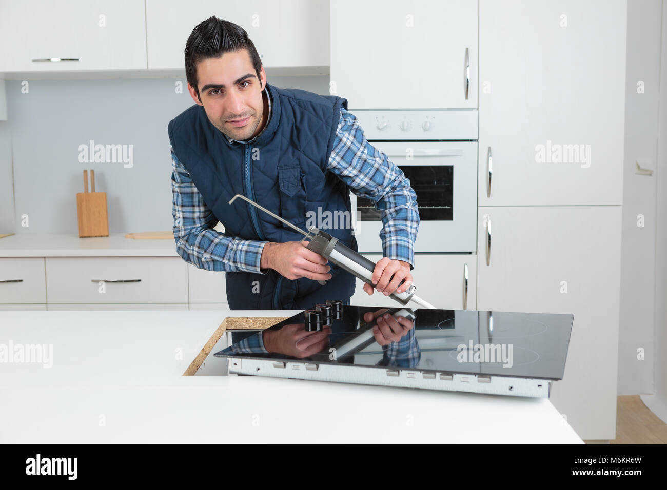 Man fitting kitchen hob, using caulking gun Stock Photo Alamy