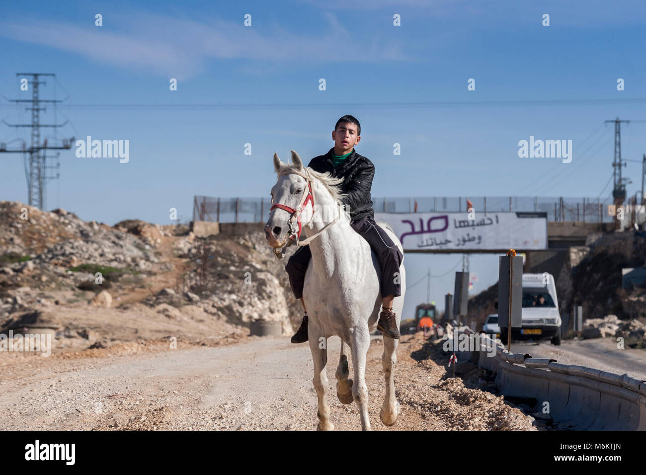 Ram, Palestine, January 12, 2011: A boy is riding a horse by a road in the messy countryside of Palestine Stock Photo