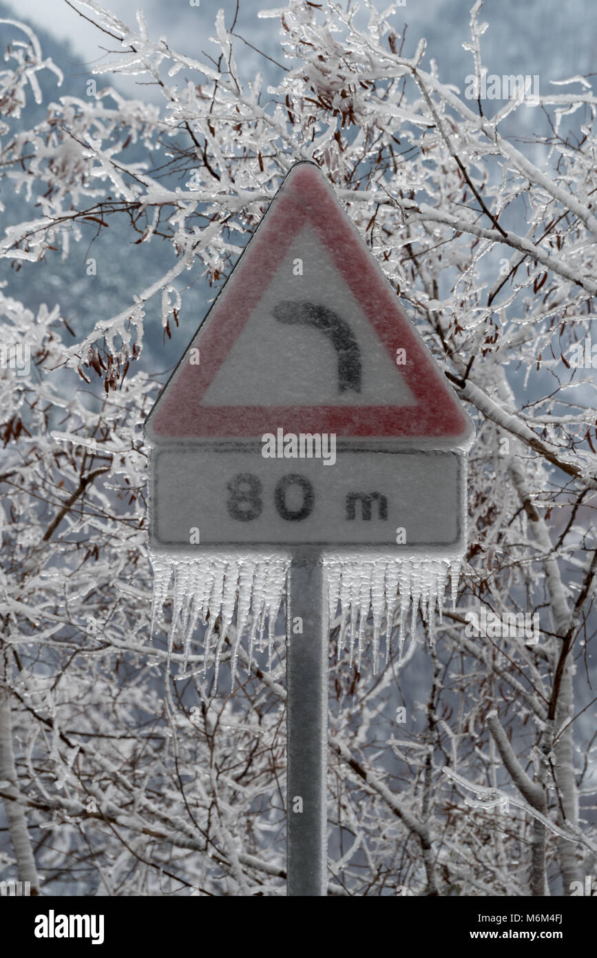 Road sign danger curve covered in ice after the freezing rain Stock Photo