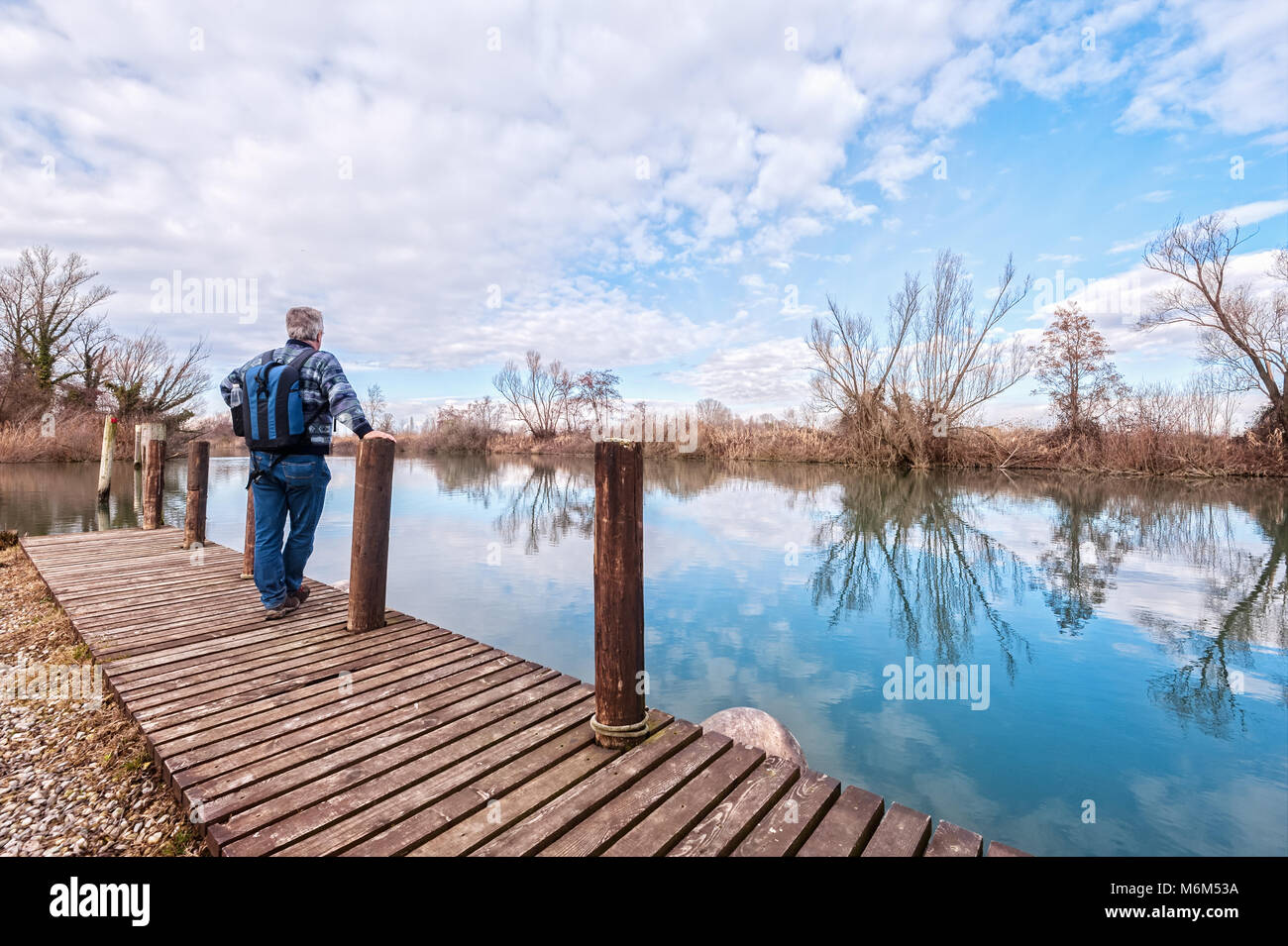 Nature landscape. Senior hiker with backpack over the wood pier on shore of river. Stock Photo