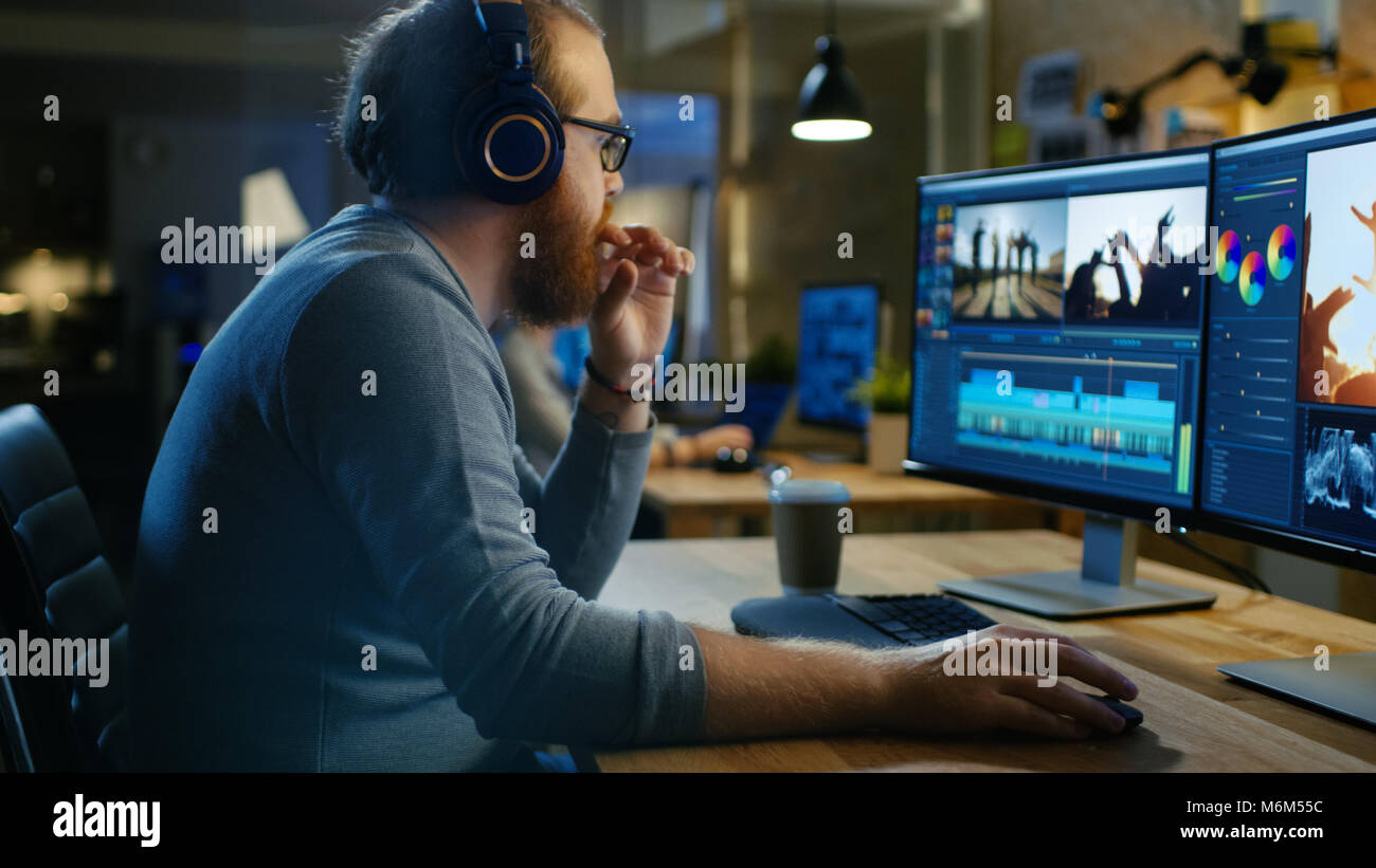 Male Videographer Edits and Cuts Footage and Sound on His Personal Computer, Puts on His Monitors/ Headphones. His Office is Modern and Creative Loft  Stock Photo