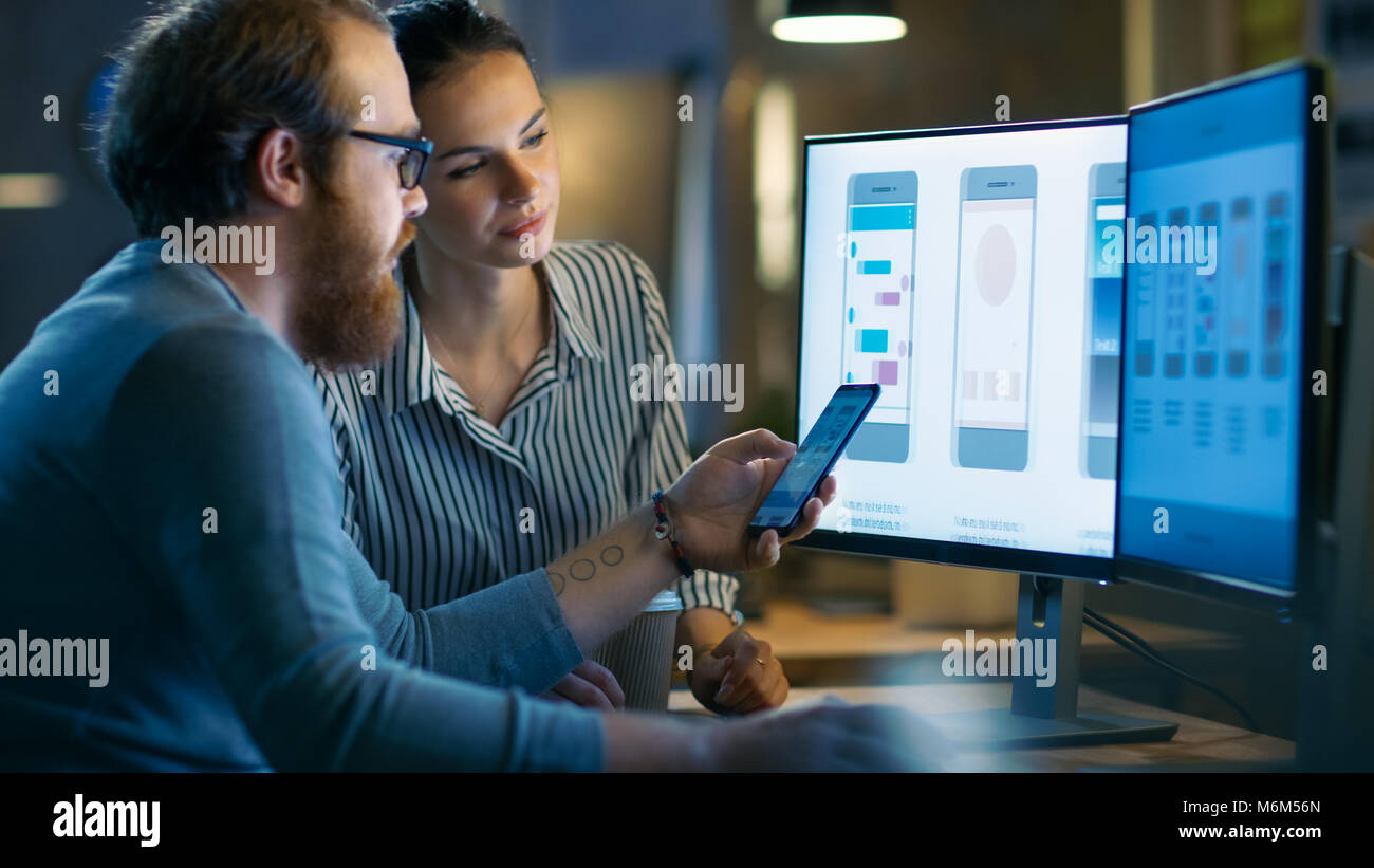 Handsome Male and Beautiful Female Mobile Application Designers Test and Discuss New App Features. They Work on a Personal Computer with Two Displays Stock Photo