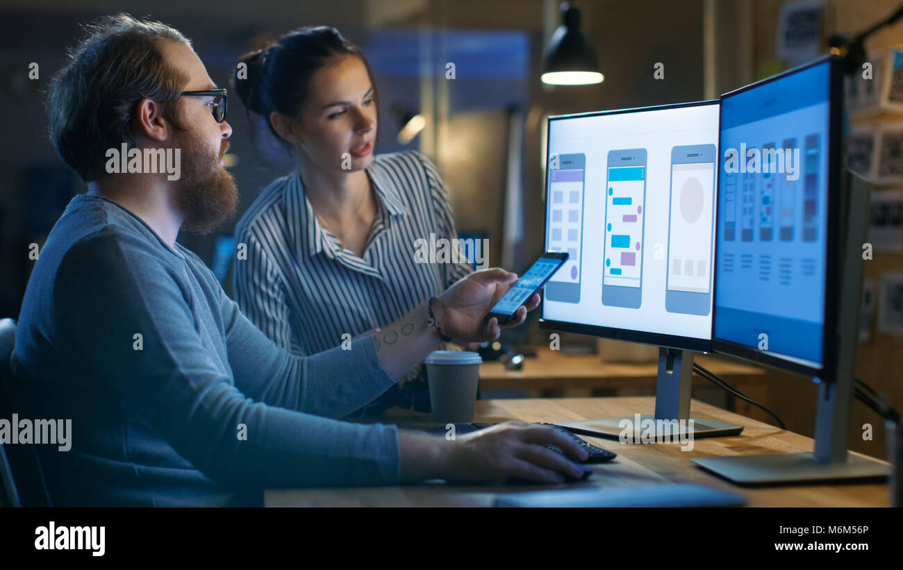 Handsome Male and Beautiful Female Mobile Application Designers Test and Discuss New App Features. They Work on a Personal Computer with Two Displays Stock Photo