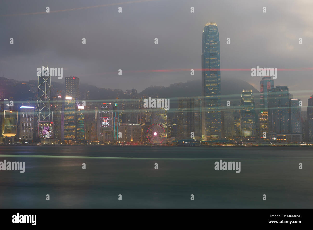 Light Trails From A Passing Boat Crossing Victoria Harbour Hong Kong At Dusk. Stock Photo