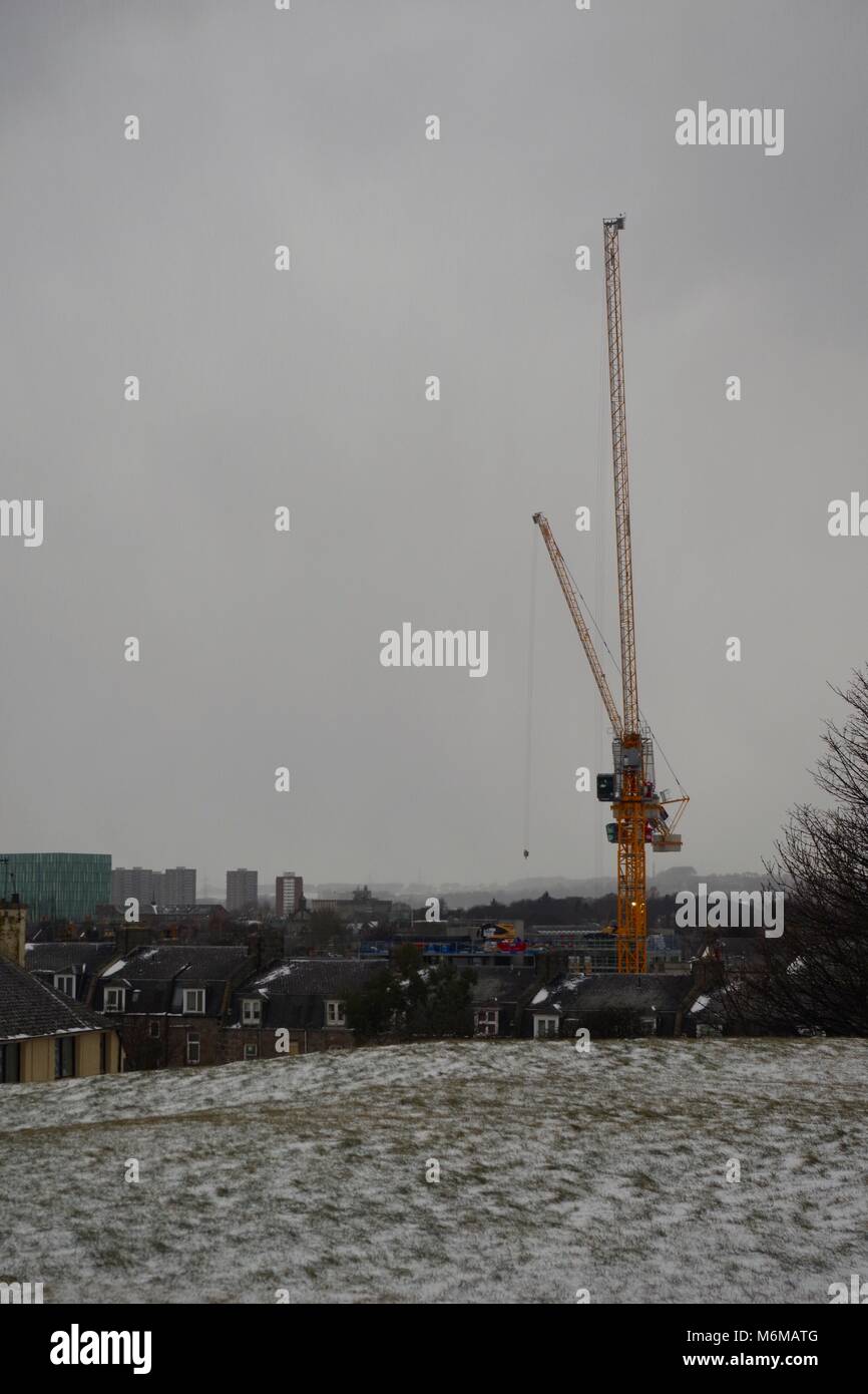 Yellow Crane on a Construction Site, Looking Towards Aberdeen University Campus on a Grey Cold Day. Beast from the East Snow Storm. Scotland UK. Stock Photo
