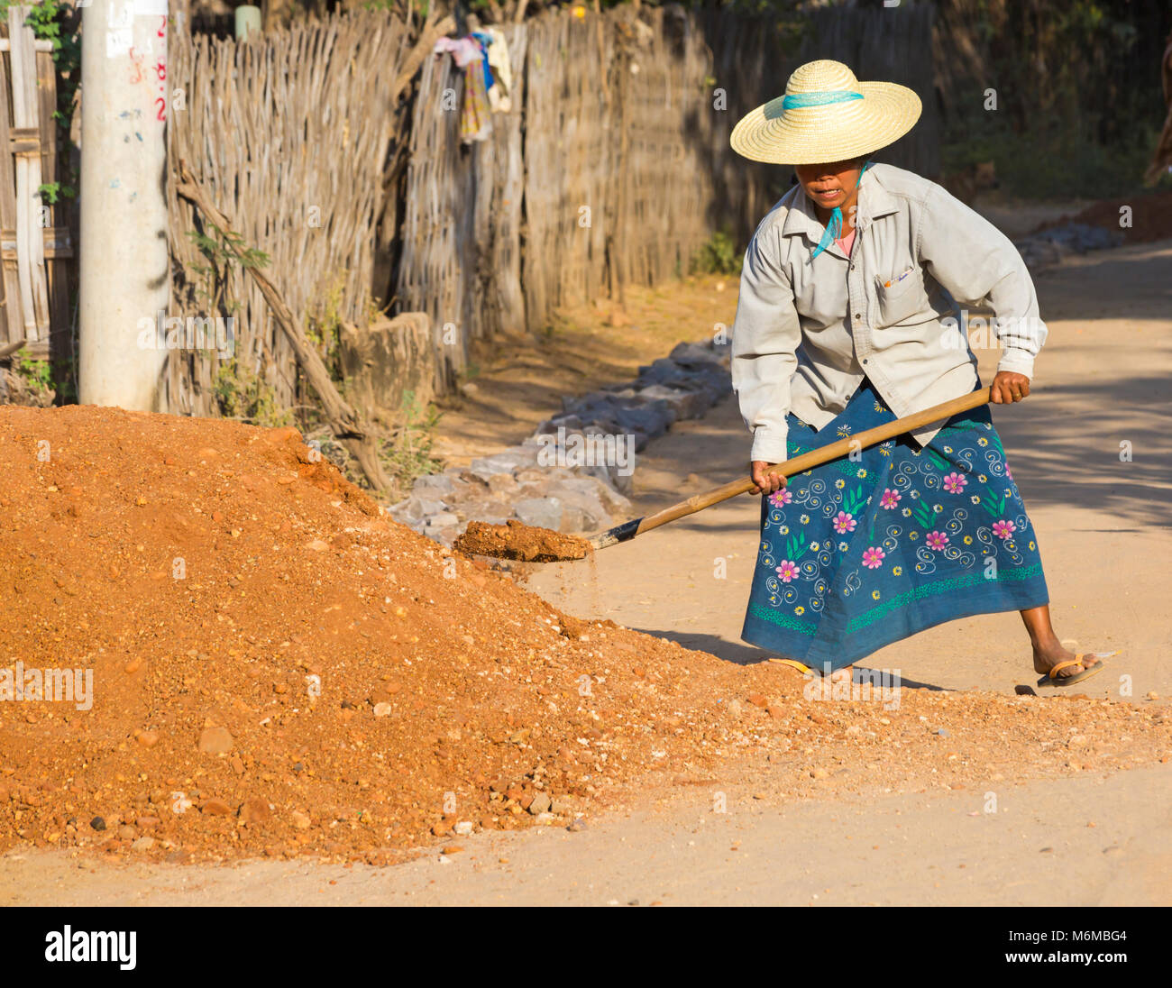 Villagers undertake manual road construction work at West Phwar Saw Village, Bagan, Myanmar (Burma), Asia in February - woman shovelling gravel Stock Photo