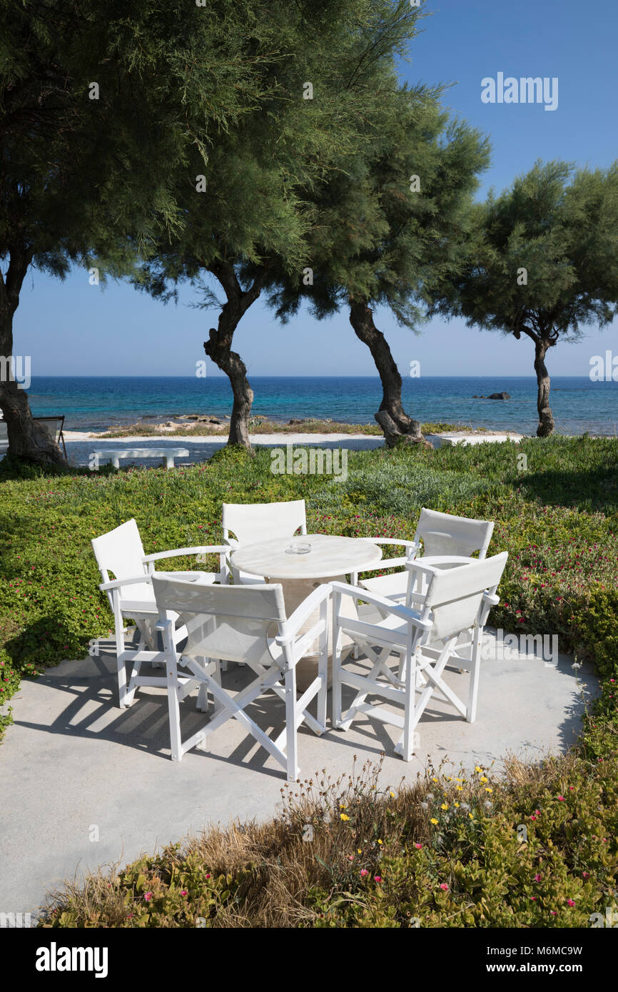 White garden table and chairs beside the sea at Nefeli Sunset Studios, Pollonia, Milos, Cyclades, Aegean Sea, Greek Islands; Greece; Europe Stock Photo